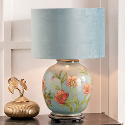Decorative Jenny Worrall glass table lamp with floral design and blue shade on a surface.