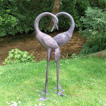 Two metal cranes garden sculptures forming a heart shape in a garden setting