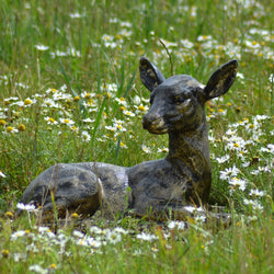 Statue of a lying metal fawn sculpture in a field with flowers